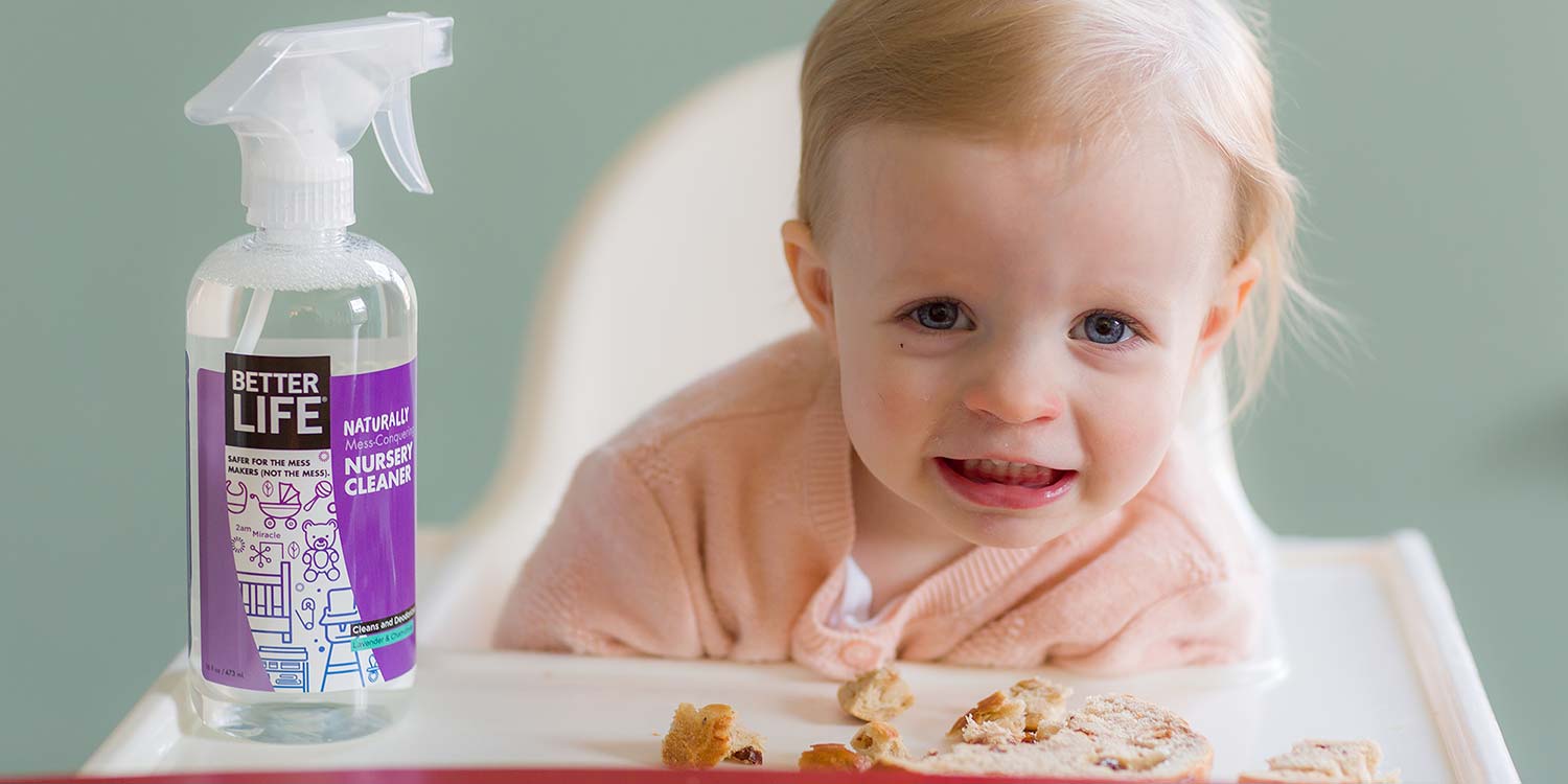 A baby smiling while eating some cereal featuring Better Life's Nursery Cleaner sitting next to the child