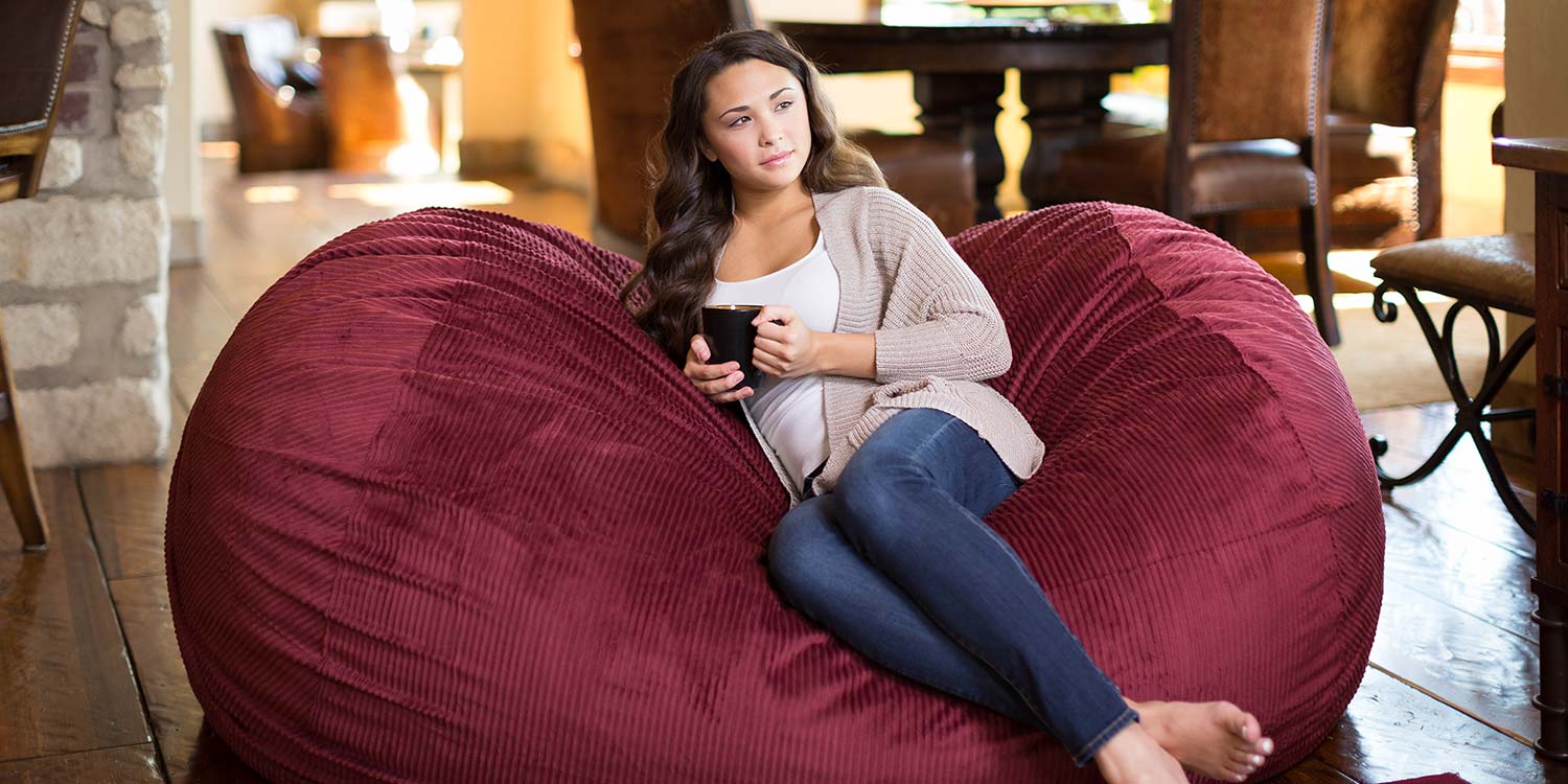 An image of a woman resting on a Comfy Sack while enjoying a nice cup of coffee