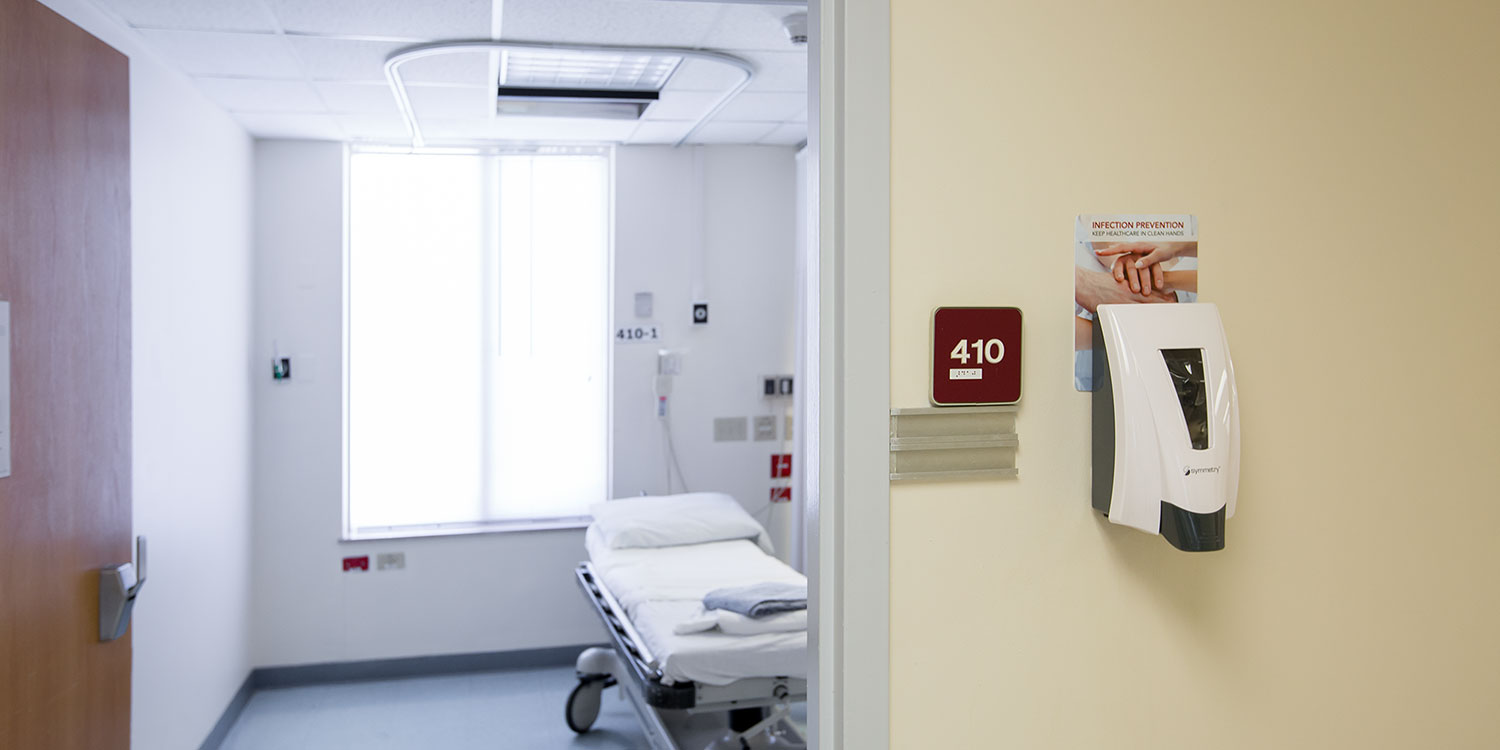 An image of a Symmetry Soap Dispenser hanging on a wall right outside a patient's room inside a hospital